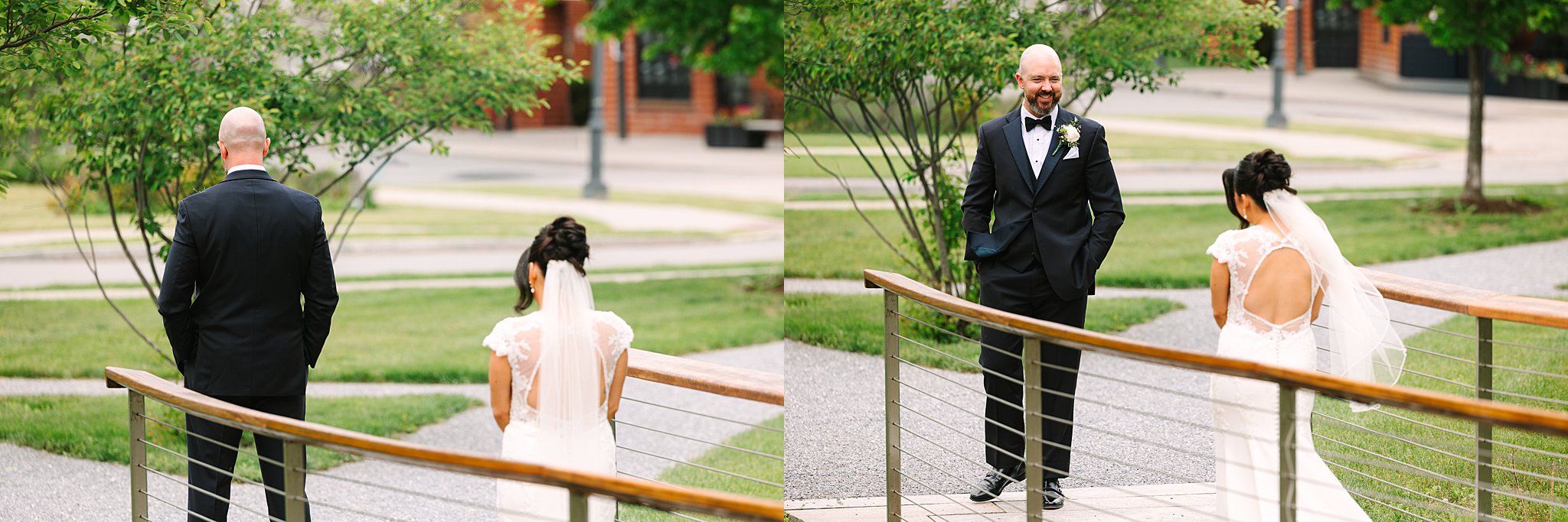 A bride in a white dress walks up behind a groom in a dark suit for a first look. In the next moment, he turns around and smiles joyfully at her on a wooden bridge outdoors.