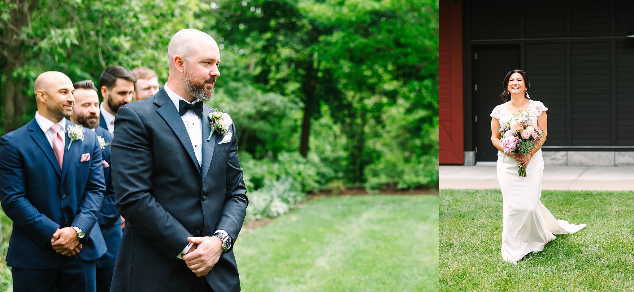 A groom in a tuxedo stands outdoors with groomsmen behind him, looking ahead, while a bride in a white dress walks toward him, smiling and holding a bouquet, with greenery and a building in the background.