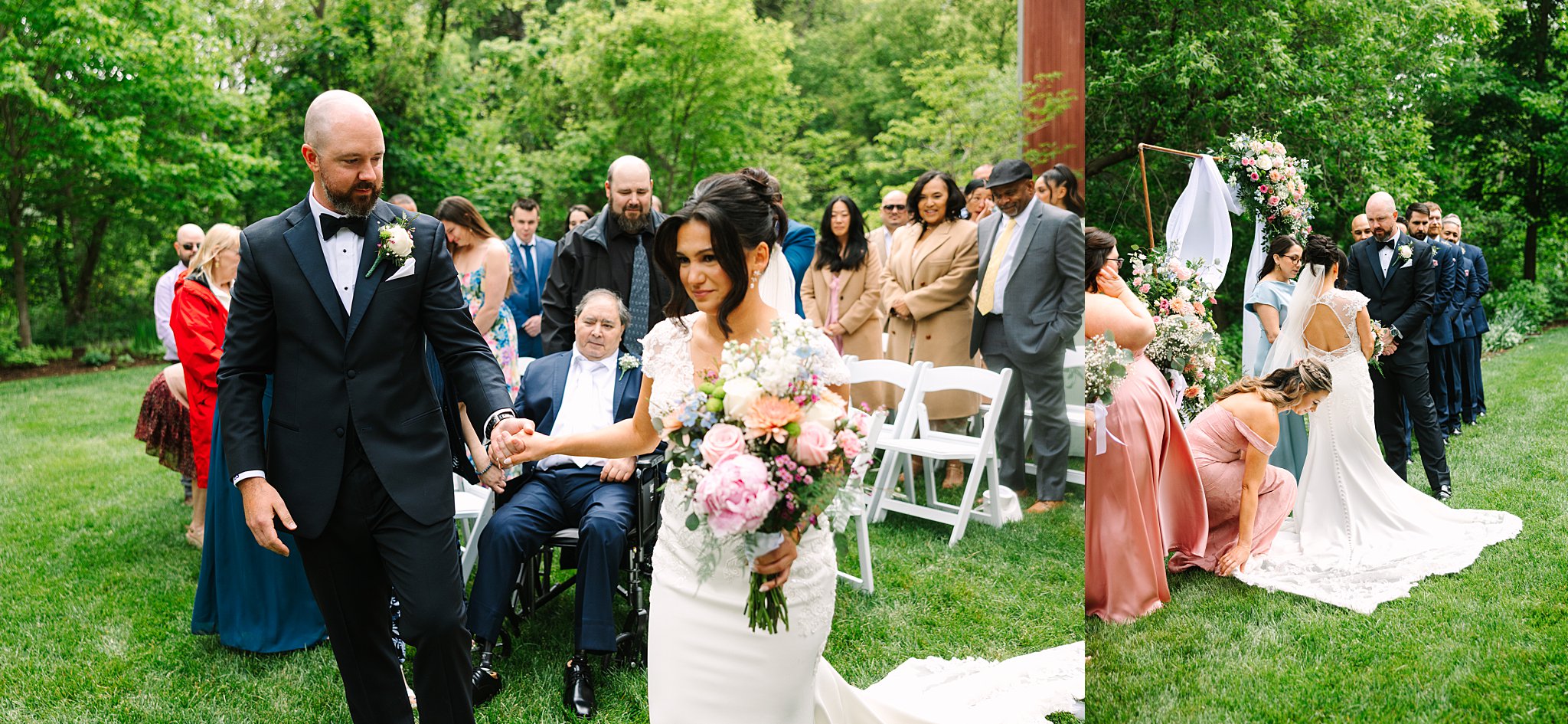 A bride and groom walk hand in hand down an outdoor aisle, surrounded by guests in formal attire. The bride holds a bouquet, and bridesmaids adjust her train on the grass, with greenery in the background.