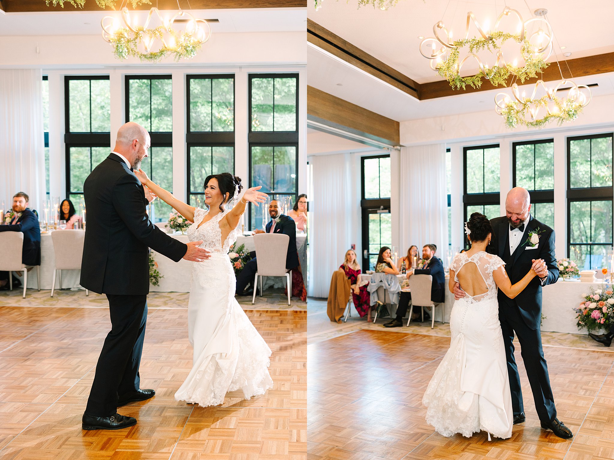 A bride and groom share their first dance at their wedding reception in a bright, elegant hall with large windows. Guests sit at tables watching and smiling in the background.