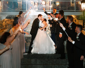bride and groom kiss surrounded by wedding party holding sparklers on the stairs at Grand View Mendon MA