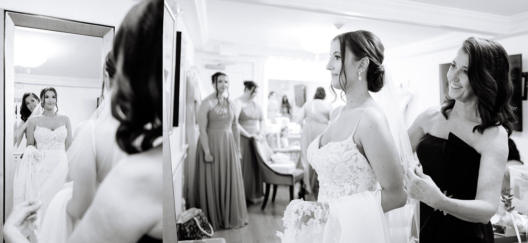 A bride in a wedding dress stands in front of a mirror, smiling as another woman helps her with her gown. Bridesmaids in dresses chat in the background. The scene is bright and joyful in black and white.