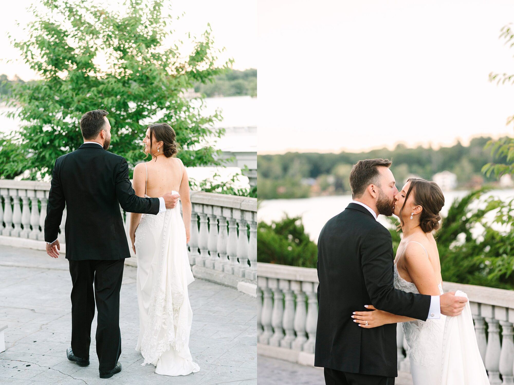 A bride and groom in formal attire share a romantic moment outdoors by a stone railing, with greenery and water in the background. The groom wears a black suit; the bride wears a strapless white gown.