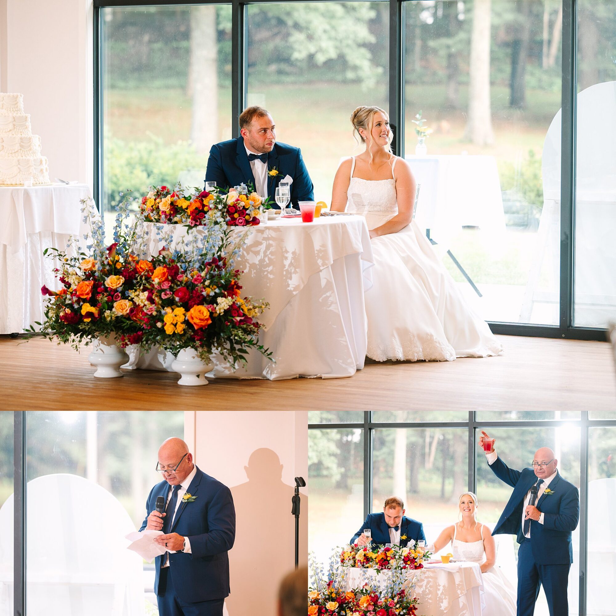 A bride and groom sit at a floral-decorated table, smiling. A man in a suit gives a speech, then raises a glass in a toast. Large windows reveal trees outside.