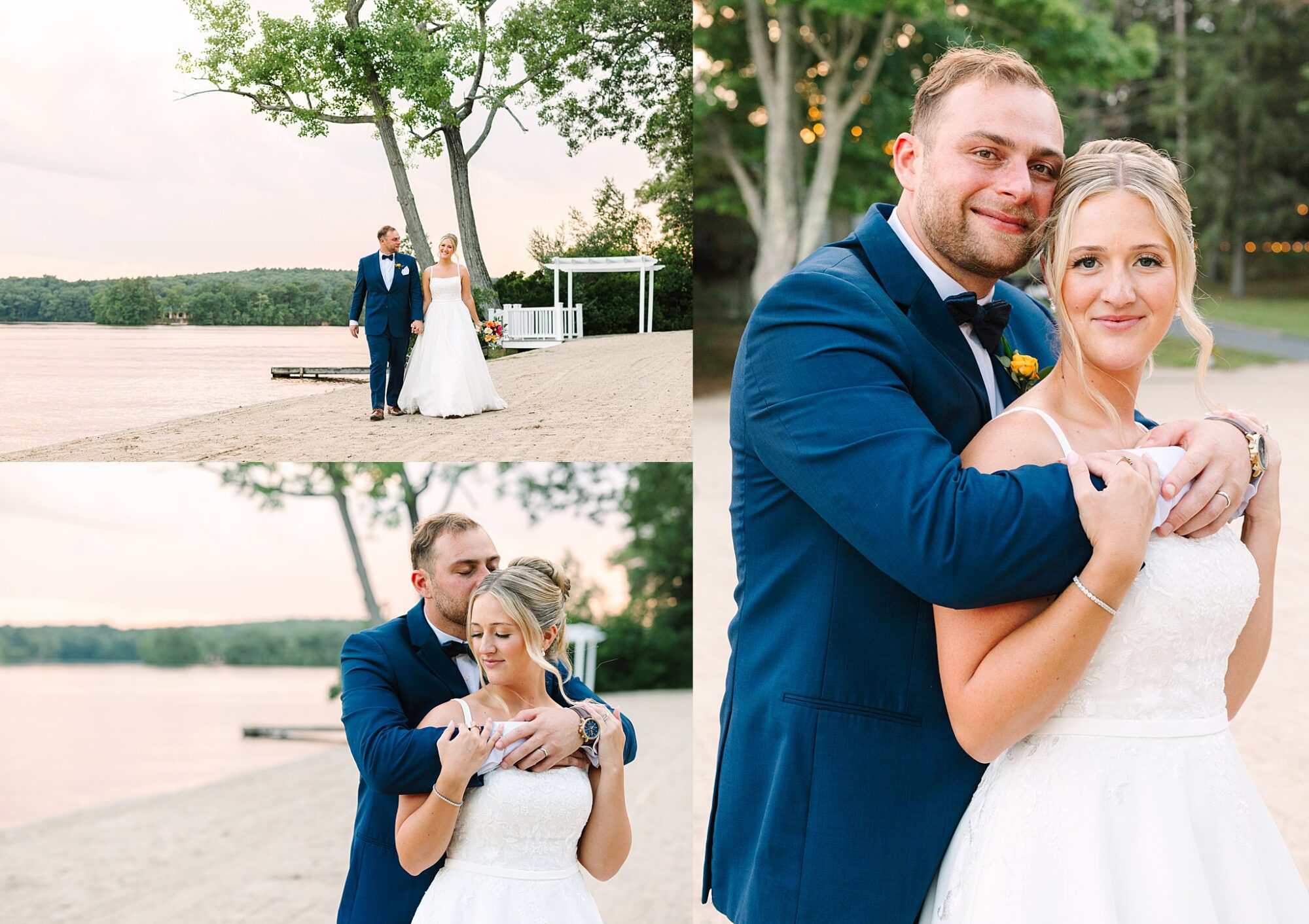 A bride and groom pose together on a sandy lakeside. The groom wears a blue suit, and the bride wears a white dress. They smile and embrace, surrounded by trees and calm water in the background.
