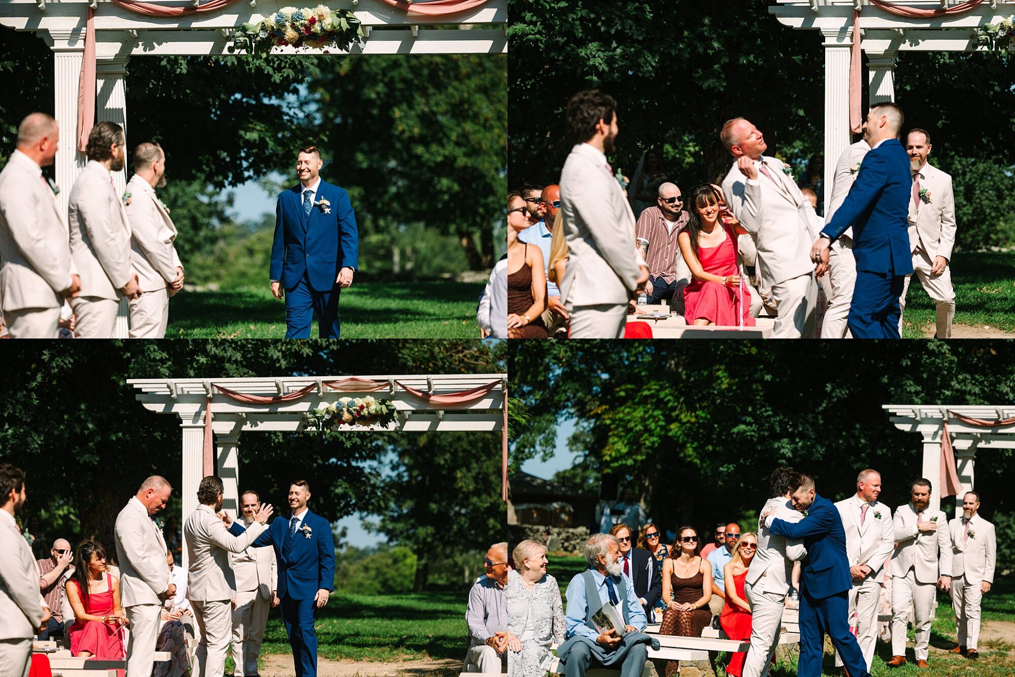 A groom in a blue suit hugs and greets groomsmen in beige suits during an outdoor wedding ceremony, with seated guests watching and smiling.