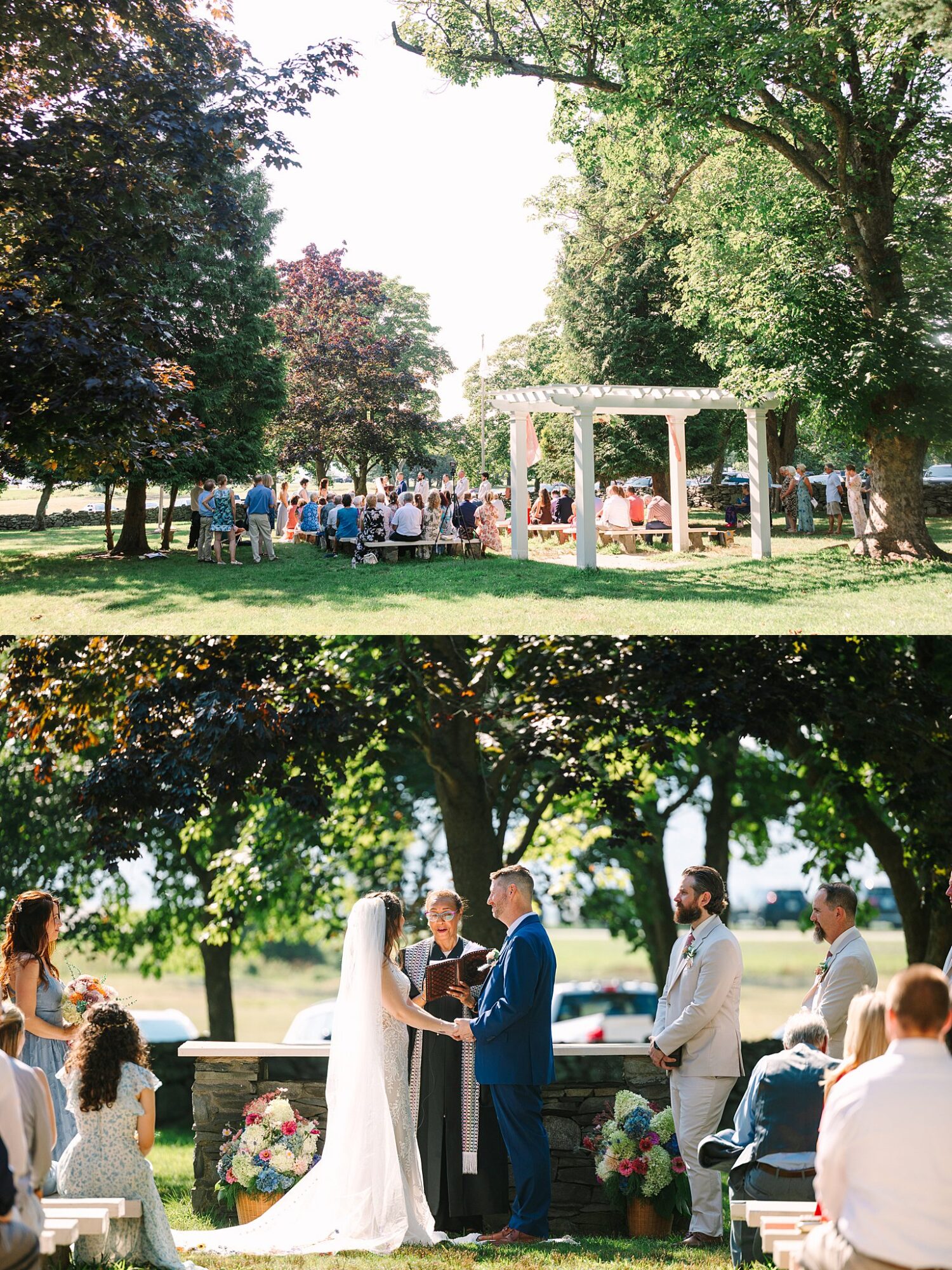 A sunny outdoor wedding with guests seated under trees. The ceremony features a bride in a veil and a groom in blue, standing before an officiant near floral arrangements and a stone wall.
