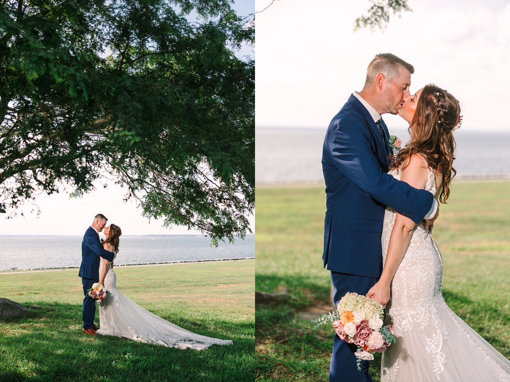 A bride and groom embrace and kiss outdoors near water, standing on grass under a large tree. The bride holds a bouquet of flowers, and both wear formal wedding attire.