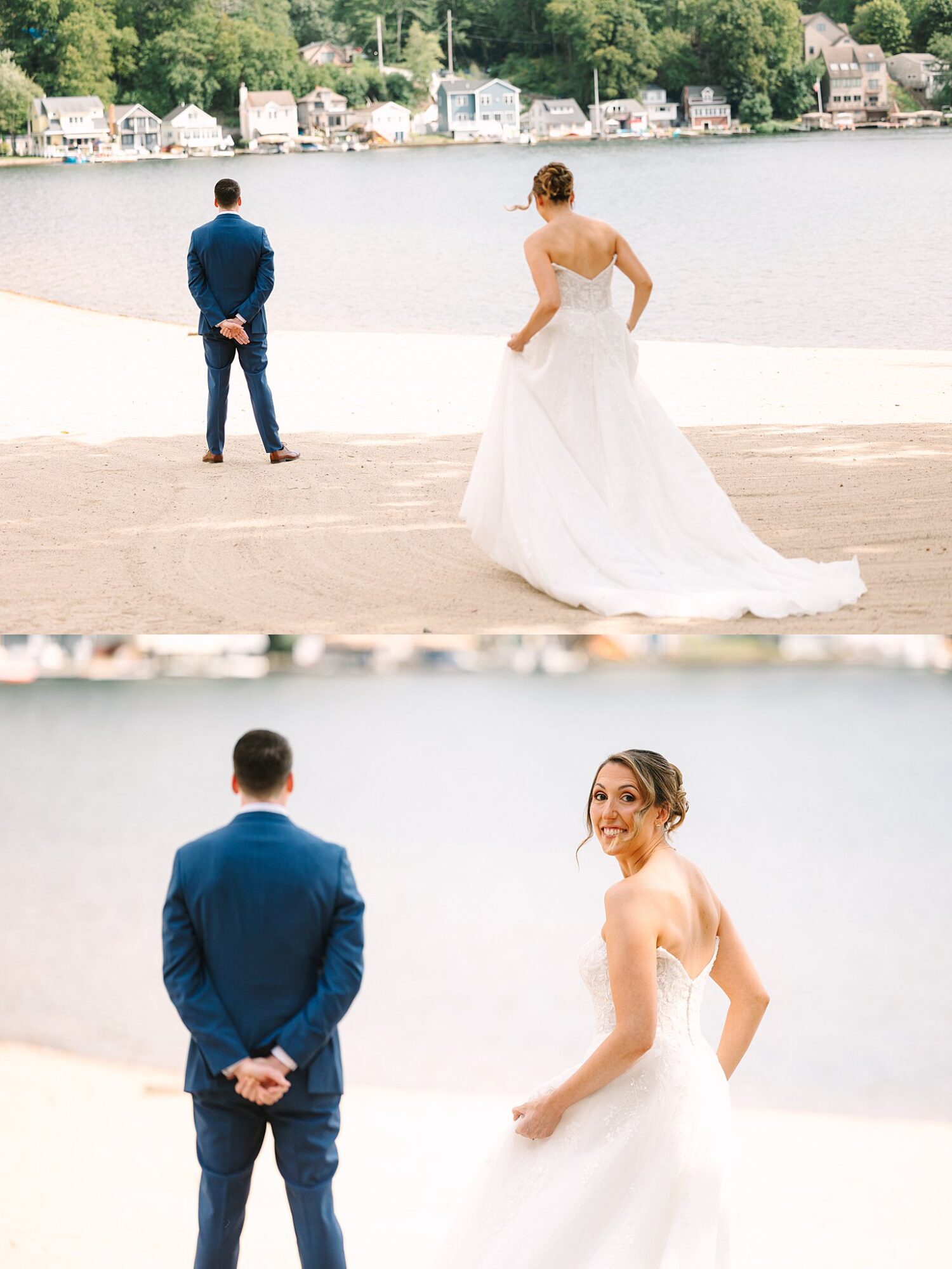 A bride in a white gown approaches a groom in a blue suit who stands with his back to her by a lakeshore, with houses and trees in the background.