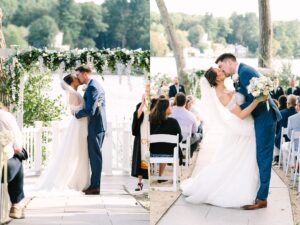 A bride and groom kiss under a floral arch during an outdoor wedding ceremony by a lake, surrounded by guests seated on white chairs.