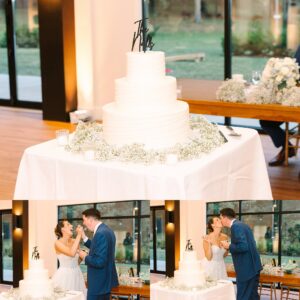 A three-tiered white wedding cake on a table, decorated with babys breath, with a bride and groom playfully feeding each other cake at their reception.